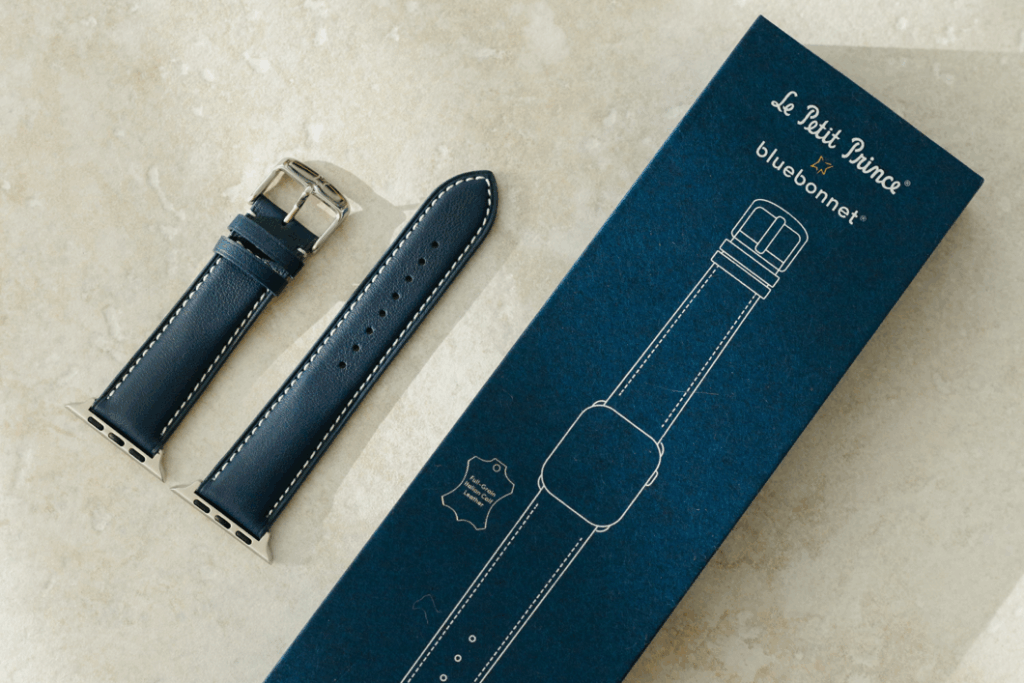Le Petit Prince x Bluebonnet Italian leather Apple Watch band in Midnight Blue, shown alongside its navy packaging with white line art illustration of the band.
