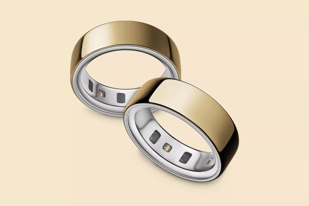 Two sleek gold smart rings with a silver interior featuring embedded sensors, displayed on a light beige background.