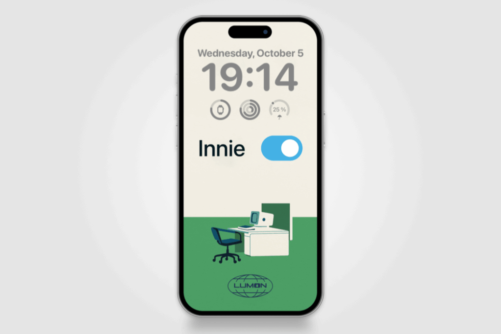 A minimalist digital illustration inspired by Severance shows a white background with a green floor. At the top, the word “Innie” appears in black next to a blue toggle switch turned on. Below, a simple office desk setup includes a white desk, an old-style computer monitor, a blue notebook, and a dark blue office chair. At the bottom center is the Lumon Industries logo, rendered in navy blue.